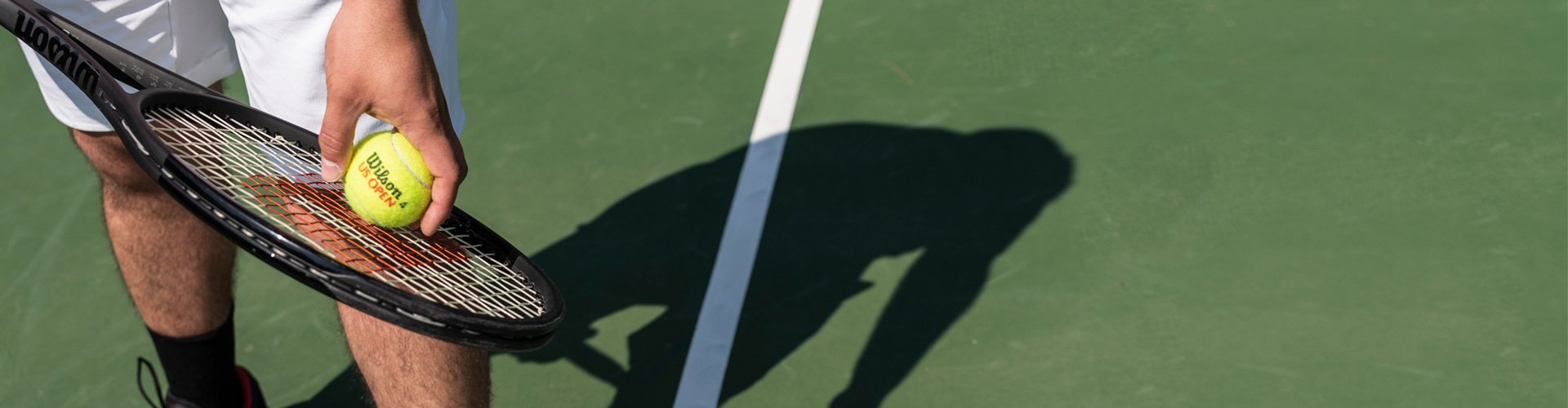 Man on tennis court holding Wilson tennis racquet and ball