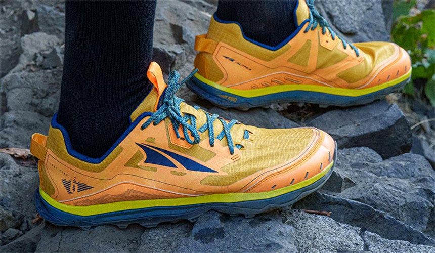 Man standing on a rock in Altra Lone Peak 6 Orange trail running shoes.