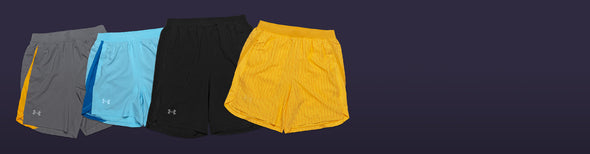 Assorted men's Under Armour Launch Run Shorts in black, blue, gray and gold displayed on a dark purple background.