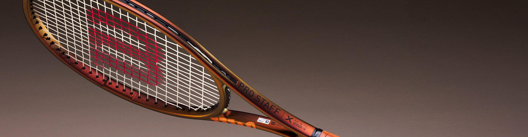 A gold-colored Wilson Pro Staff v14 tennis racquet on a gradiated background.