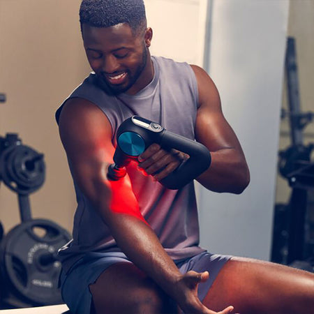 A person using a Theragun Pro Plus device on their arm, emitting red light indicating the application of near-infrared LED light therapy.