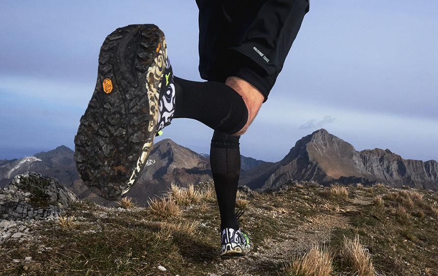 person running on a mountain trail wearing black white and green Mizuno trail running shoes