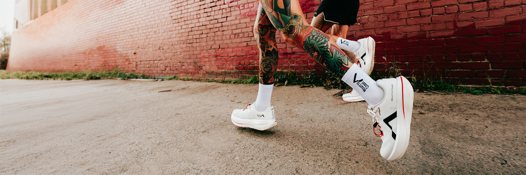 Person wearing Mount to Coast C1 running shoes on a street with a brick wall in the background.
