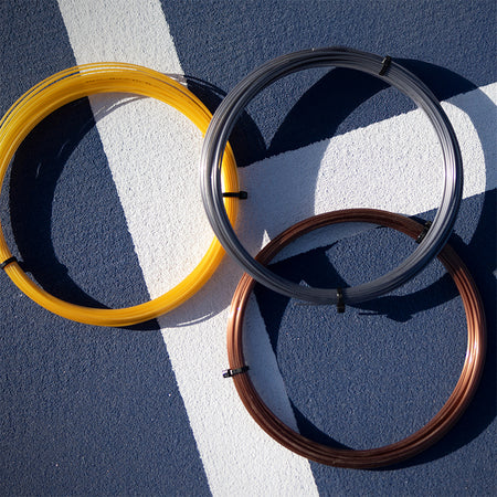 Luxilon tennis string laying on a blue tennis court.