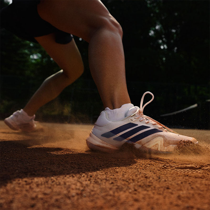 Person playing tennis on a clay court wearing white adidas Barricade 14 women's tennis shoes with dark blue accents