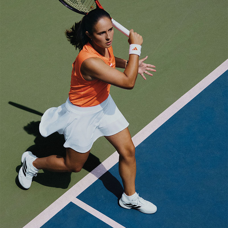 A person playing tennis wearing orange and white adidas clothing and shoes on a blue court.