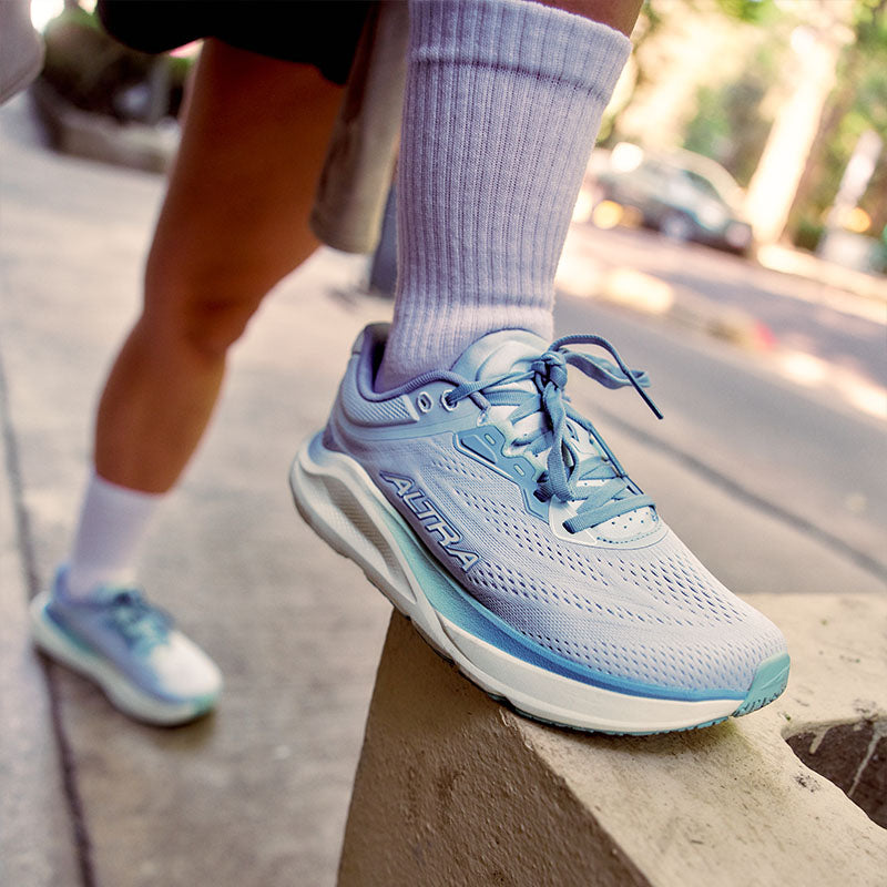 A person wearing women's Altra Torin ST running shoes stretching on a concrete structure