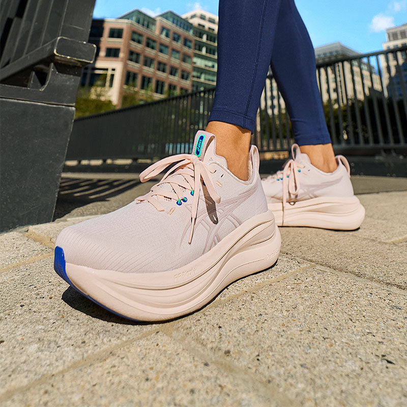 Person wearing light pink ASICS GEL-Nimbus 28 women's running shoes on a city sidewalk