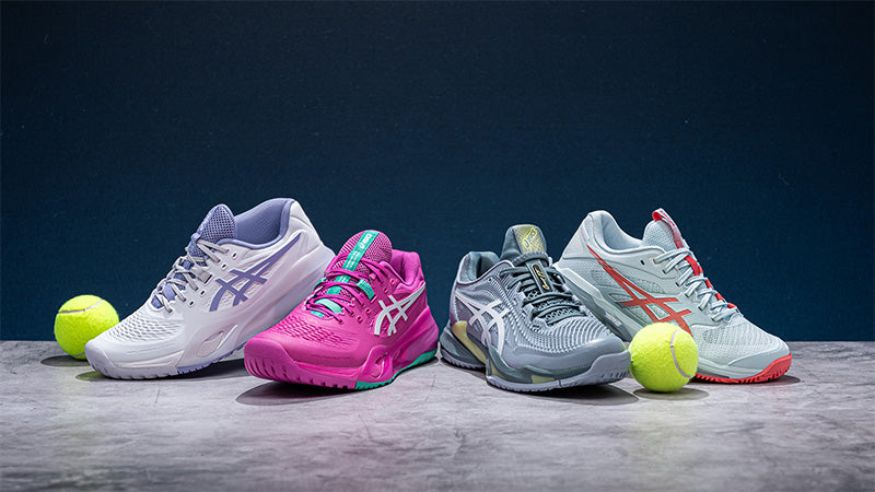 Four ASICS tennis shoes and two tennis balls posed on a gray floor against a dark blue background