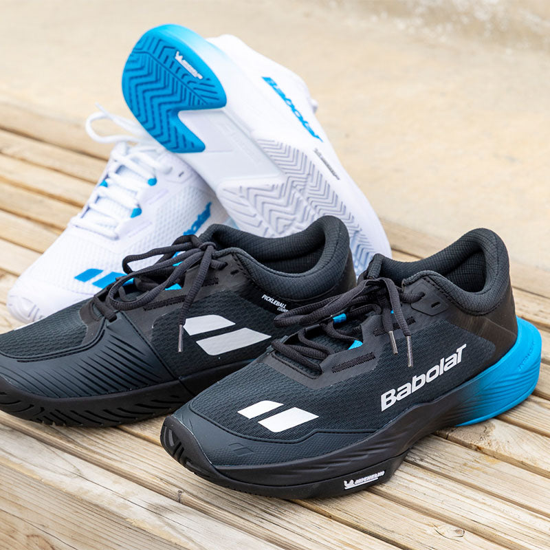 Two pairs of Babolat pickleball shoes on a wood bench surface