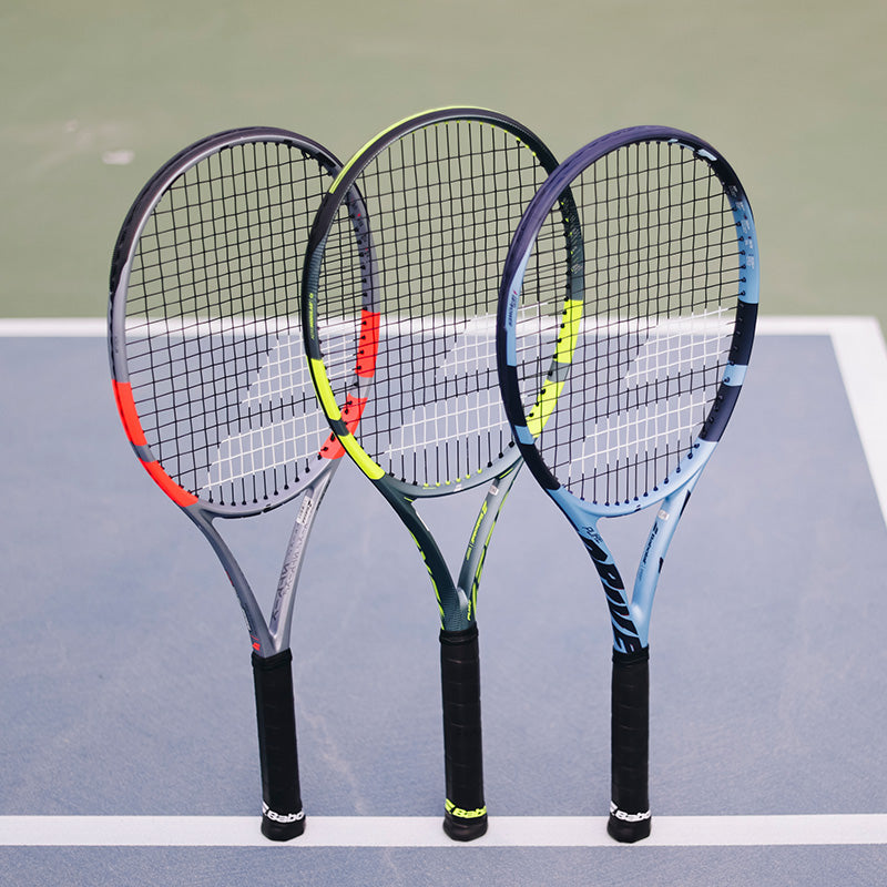 Three Babolat tennis rackets with different color frames on a tennis court.
