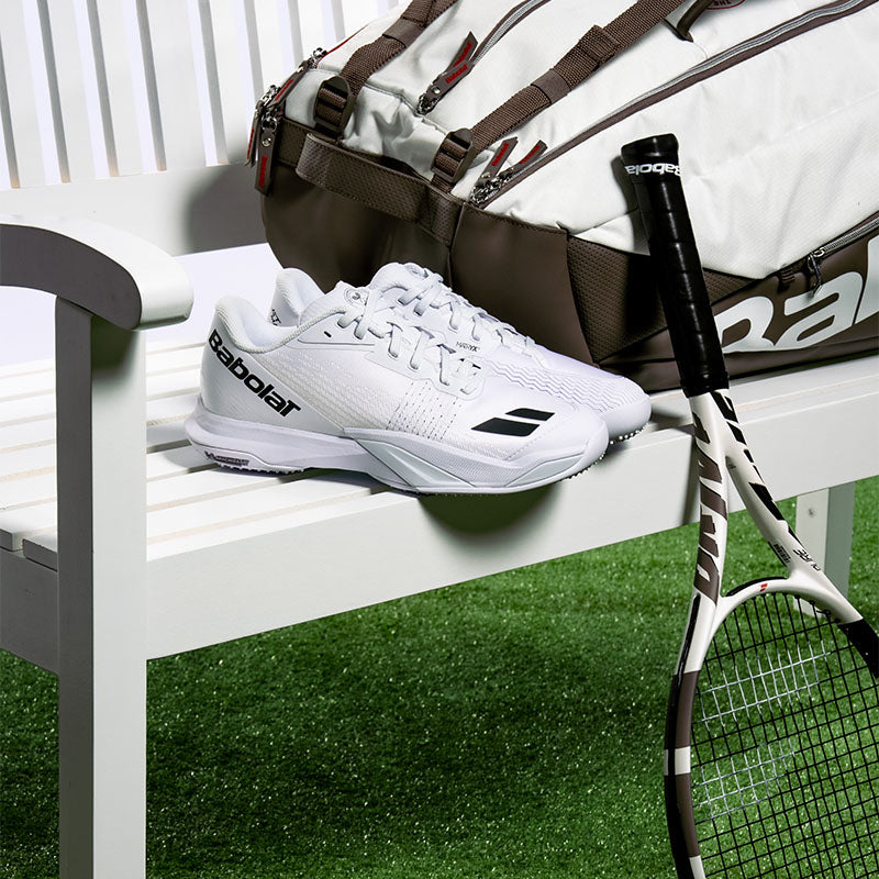 Babolat Wimbledon tennis shoes, racquet and racquet bag on a white bench on a green turf grass surface