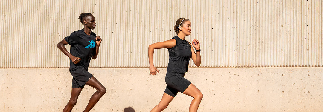 Two woman running in front of tan wall