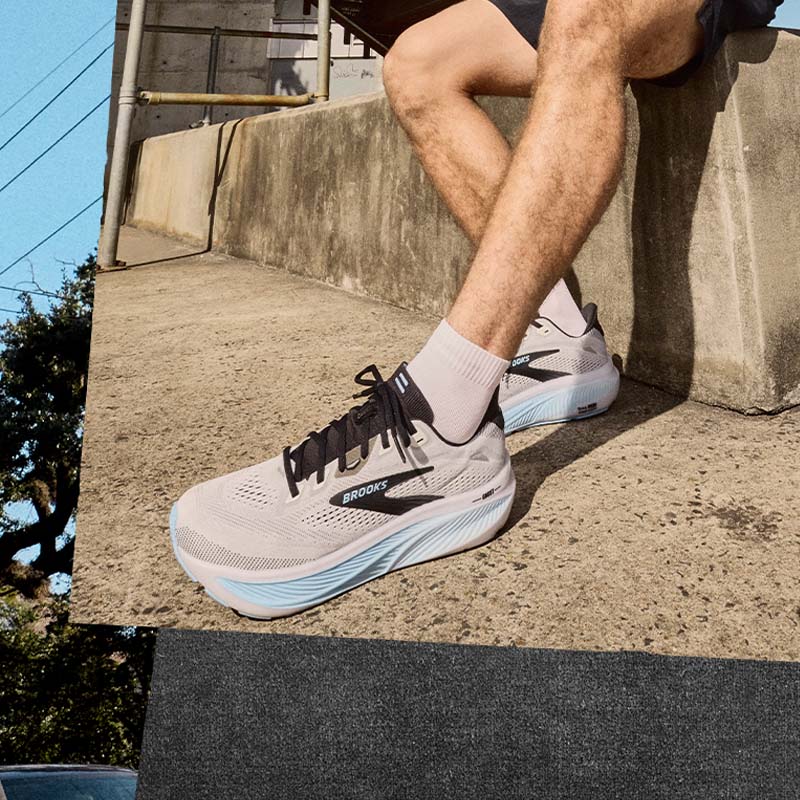 A person wearing gray and light blue Brooks Ghost 18 men's running shoes on a concrete step