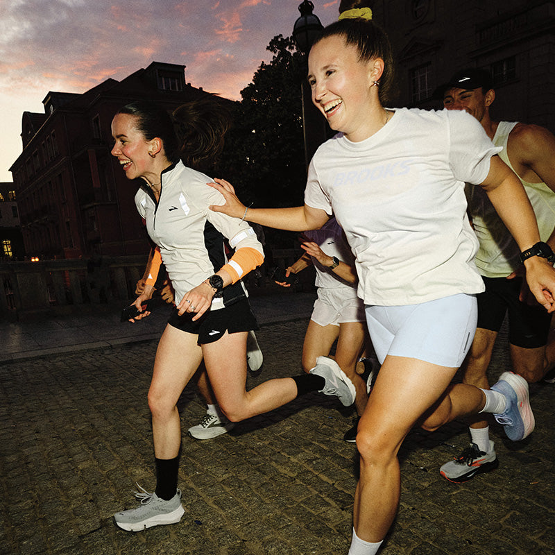 A group of runners on a cobblestone  path with two women in front wearing Brooks running clothing.