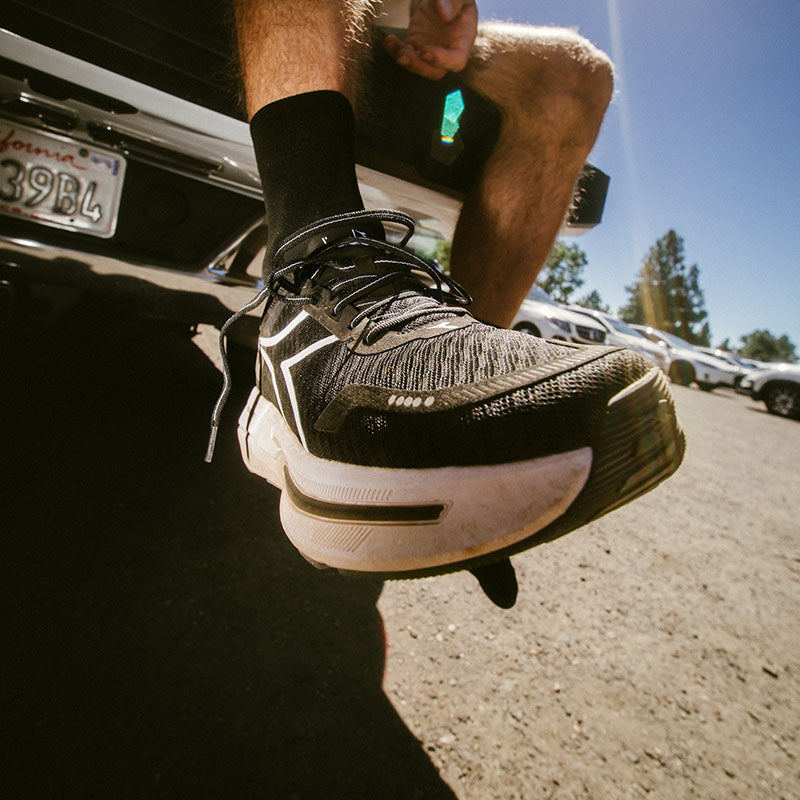 Person on a tailgate wearing black and white Diadora Cellula 2 running shoes with cars in the background.