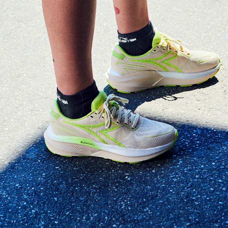 Beige and green Diadora running shoes on a person's feet on a road.