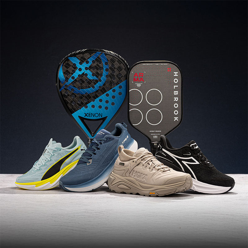 Four sports shoes, a padel racquet, and a pickleball paddle on light floor, against a dark background.