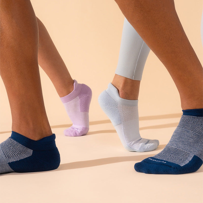 People wearing three differently colored pairs of Feetures High Performance Max Cushion No Tab Socks on a beige background.