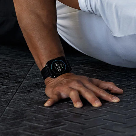 Person doing pushups while wearing a black Garmin Venu X1 Premium GPS Sportwatch on a black gym floor