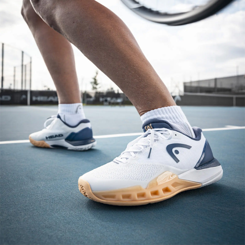 Closeup of a person playing tennis in white, blue and gold HEAD Revolt Pro 5.0 tennis shoes on a blue court
