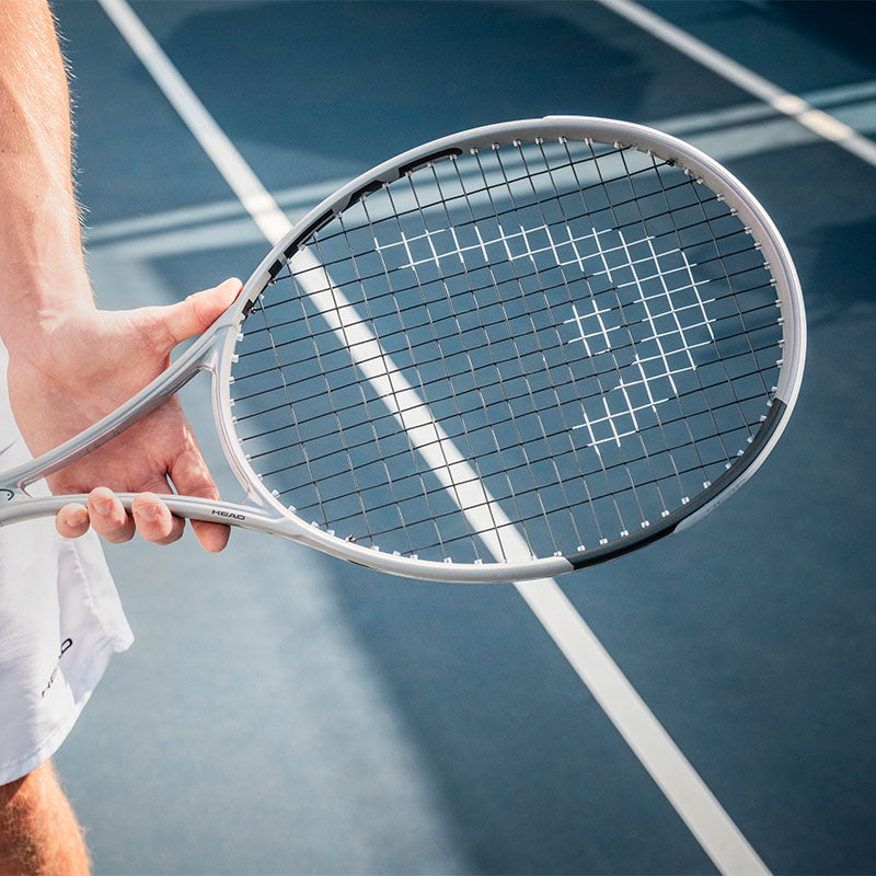 Silver colored HEAD Squared 100 tennis racquet held by a player on a blue court
