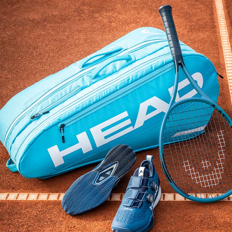 Blue HEAD Tennis Bag, Racquet and Shoes posed together on a clay court.