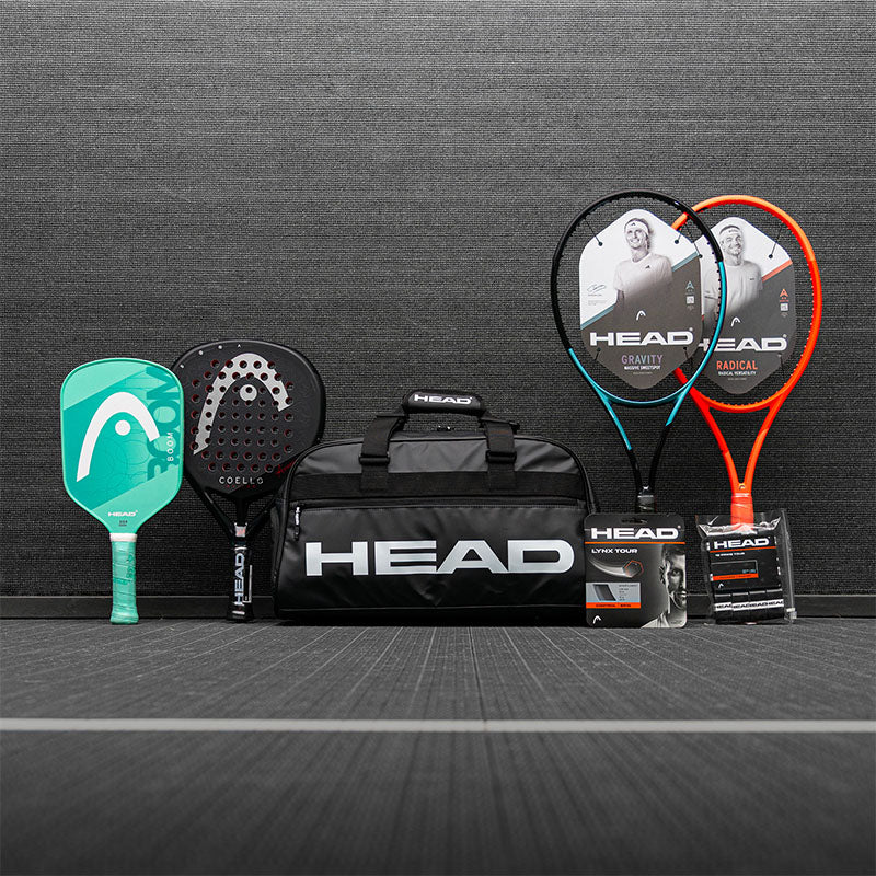 Collection of HEAD tennis, pickleball and padel sports equipment including racquets and a bag on a gray surface.