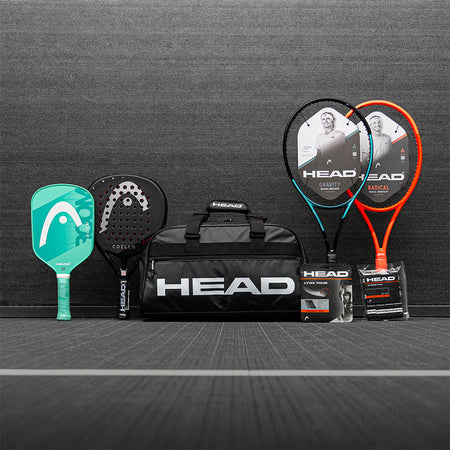 Collection of HEAD tennis, pickleball and padel sports equipment including racquets and a bag on a gray surface.