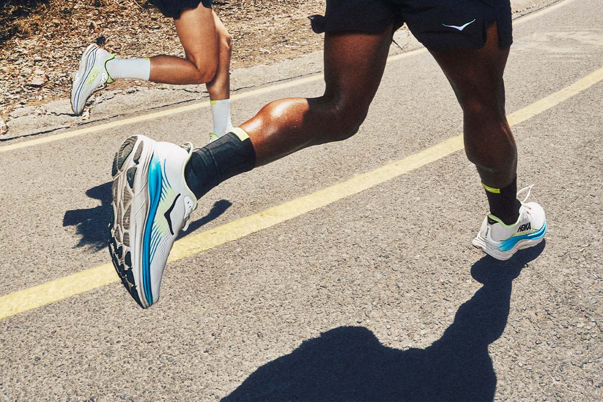 Two runners on a road wearing HOKA Clifton 1 1 running shoes.