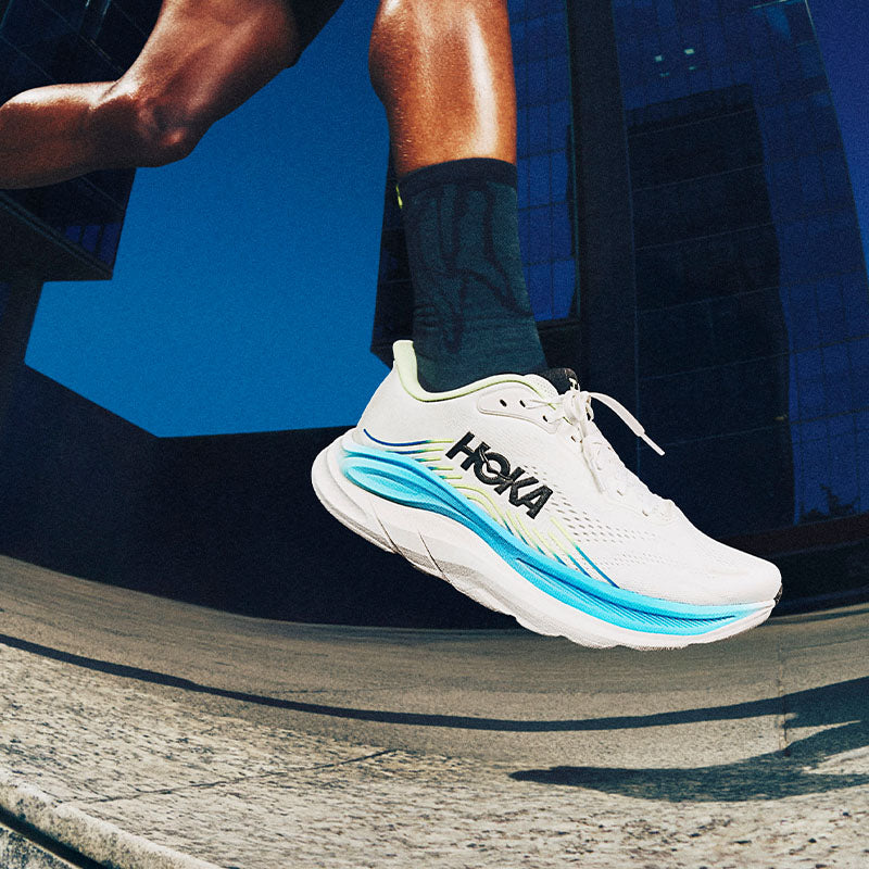 closeup of a runner wearing white and blue men's HOKA Clifton 11 running shoes on a city sidewalk