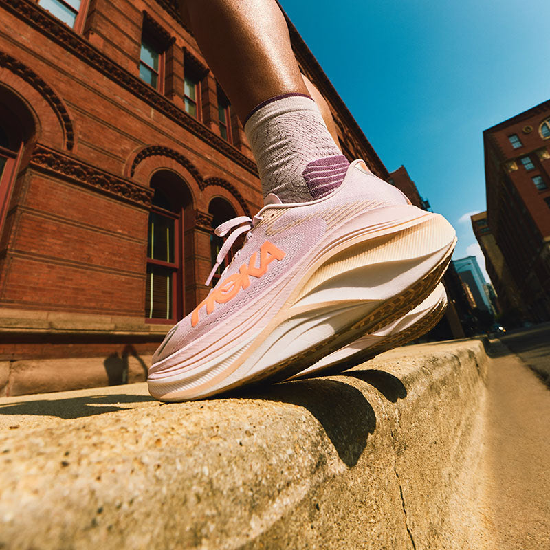 Person wearing pink HOKA Skyward X 2 women's running shoes with orange accents on a city street.