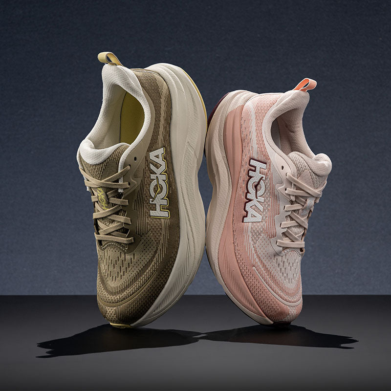 Two HOKA Skyflow running shoes shown side by side on a dark studio background. The left shoe is olive green and cream, and the right shoe is blush pink and cream.
