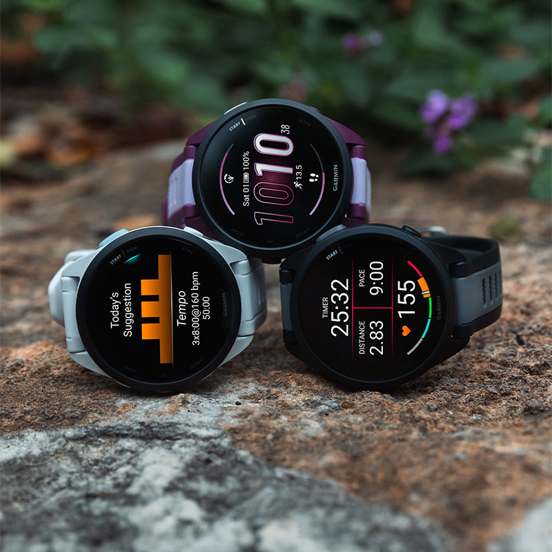  a pyramid on a forest floor.Three differently colored Garmin Forerunner 165 GPS watches stacked in