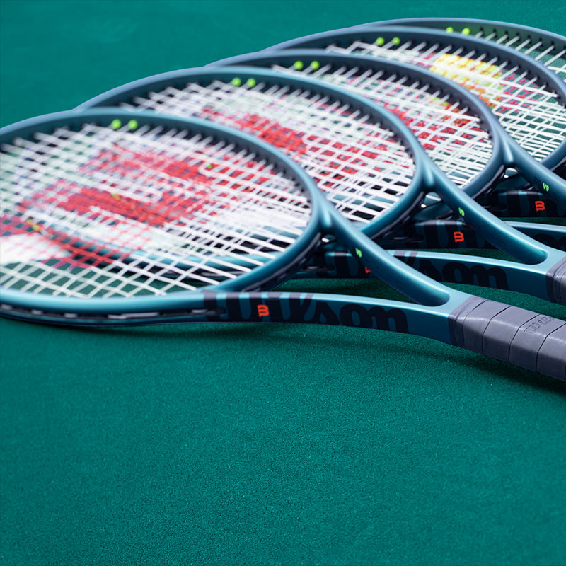 Lifestyle image: Wilson Blade V9 tennis racquets laying on a green tennis court.