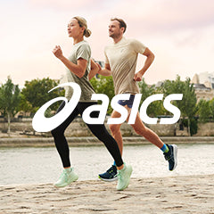 Lifestyle image: Two people running in men's and women's ASICS GEL-Nimbus 26 on a stone path along a waterfront with green trees and stone structures on the opposite side.
