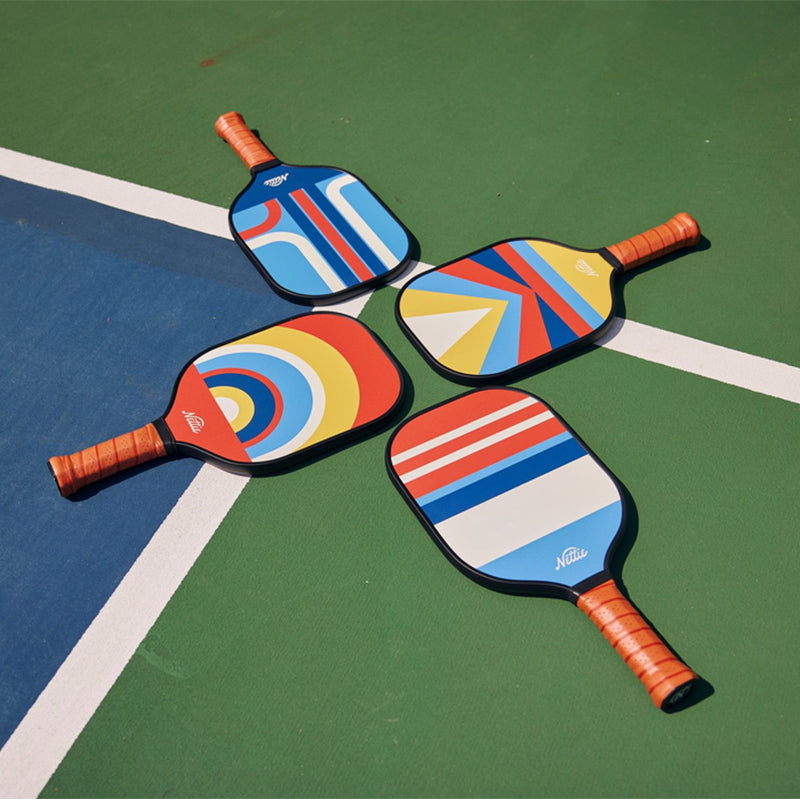 Four Nettie Classic Pickleball Paddles laying flat on a blue and green court.