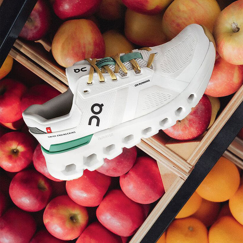 White On Cloudrunner 2 shoes sitting on top of fruit crates containing red apples and oranges