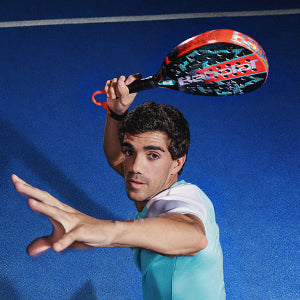 A man playing Padel on a blue court with a Babolat paddle.