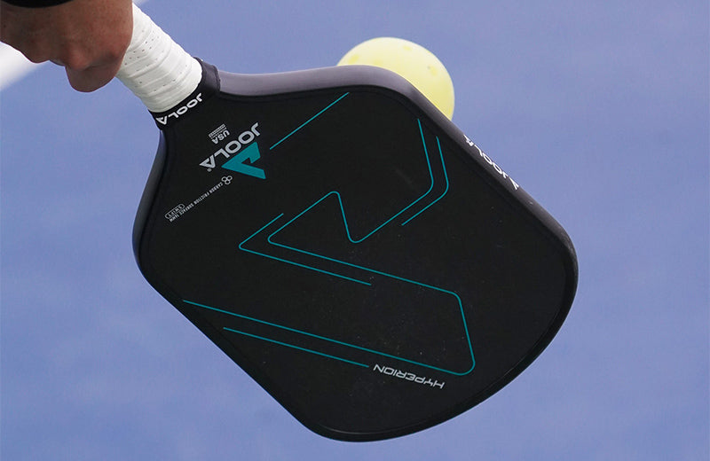Closeup of a person hitting a pickleball with a JOOLA paddle.