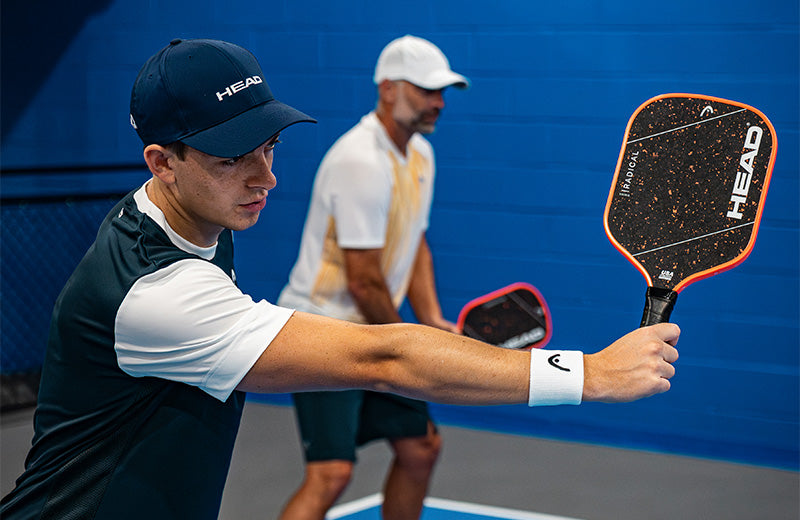 A player holding a HEAD Radical pickleball paddle on a court with another player in the background.