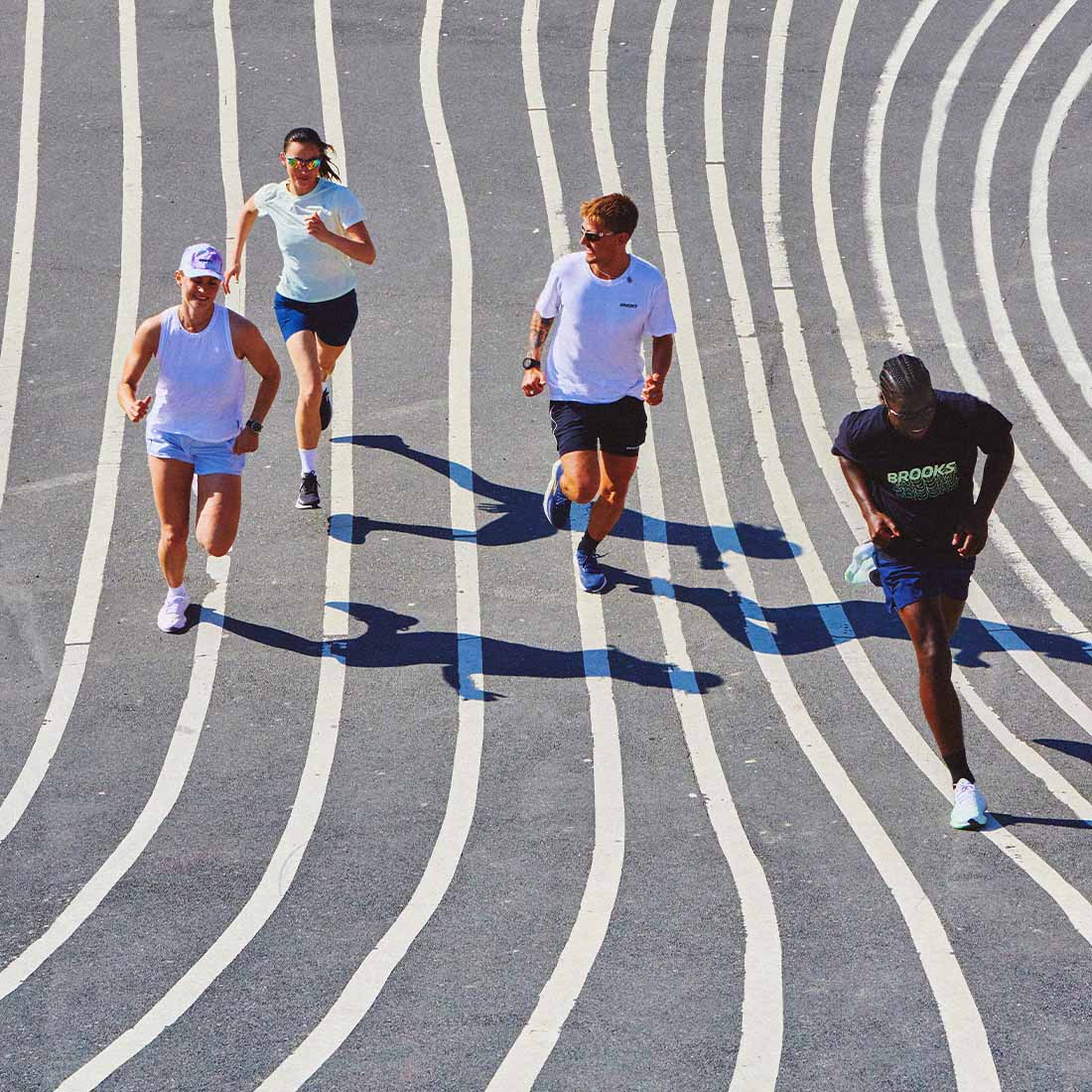 Four runners wearing Brooks shoes and clothing on a running track with white lines