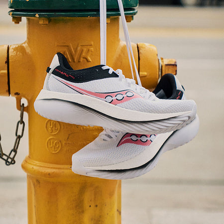White, black and red Saucony Kinvara Pro running shoes hanging from a yellow fire hydrant. 
