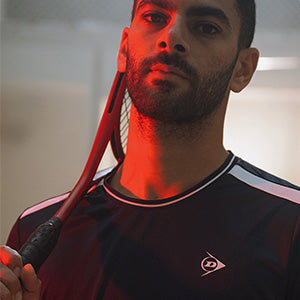 Man holding a squash racket with a red hue