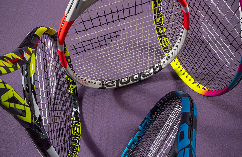 Babolat Pure Drive, Strike, Aero, and Rafa tennis racquets shot at a downward angle on a purple tennis court.