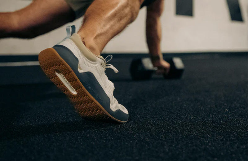 Person exercising with dumbbells wearing Year of Ours training shoes on a gym floor.