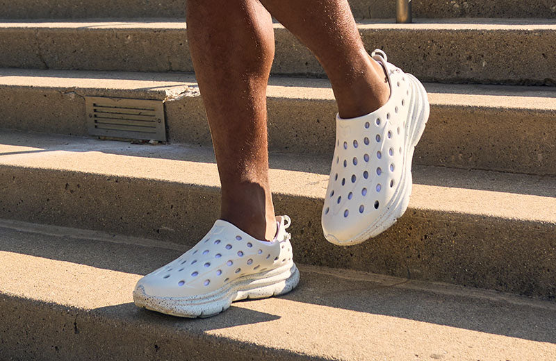Person in cloud gray and speckled purple Kane walking shoes on concrete steps