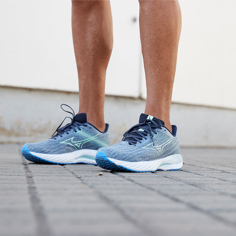 Blue Mizuno Wave Inspire 21 running shoes with white soles on a person's feet, standing on a paved surface.