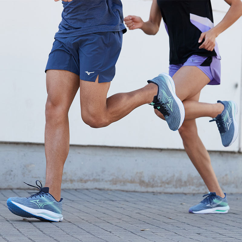 Two people running on a sidewalk wearing blue Mizuno Wave Inspire 21 running shoes.