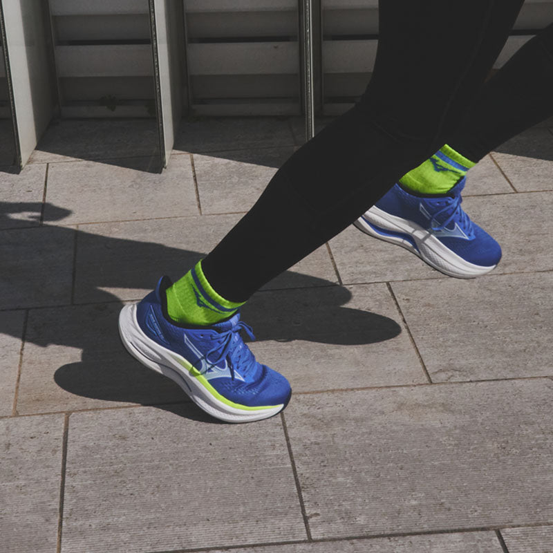 Person wearing blue Mizuno Wave Inspire 22 women's running shoes with green accents and socks running on a paved surface